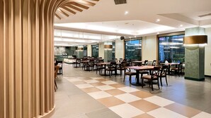A spacious dining area with checkered flooring, multiple tables and chairs, and a large window offering a view of the outdoors. - Uni-Resort Mawutu (Guanxi)