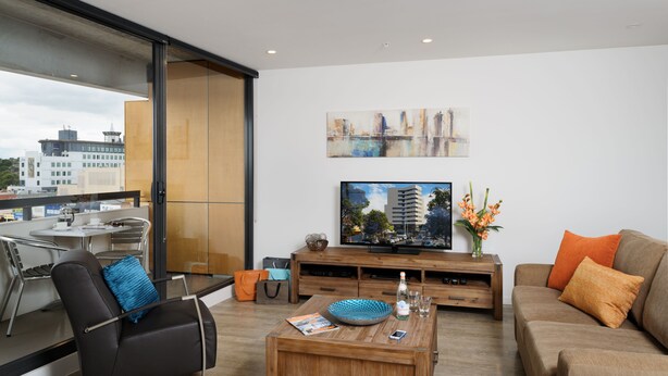 A modern living room with a large TV, comfortable seating, a coffee table, and a view of the city through large windows. - Park Avenue - IKON Glen Waverley (Glen Waverley)