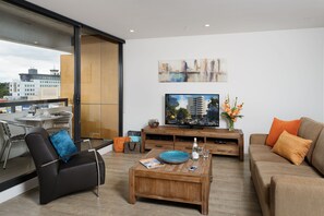 A modern living room with a large TV, comfortable seating, a coffee table, and a view of the city through large windows. - Park Avenue - IKON Glen Waverley (Glen Waverley)