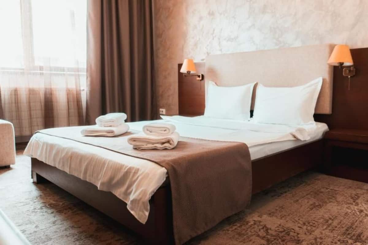 Una habitación de hotel con una cama, dos lámparas de noche, una mesita de noche y una ventana con cortinas.