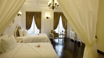 Ein Hotelzimmer mit zwei Betten, einer Kandelaber, einem Sessel und einem kleinen Tisch mit einer Lampe.