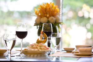 A dining table with a plate of food, wine glasses, and a vase of flowers. - Eldora Hotel (Hue)