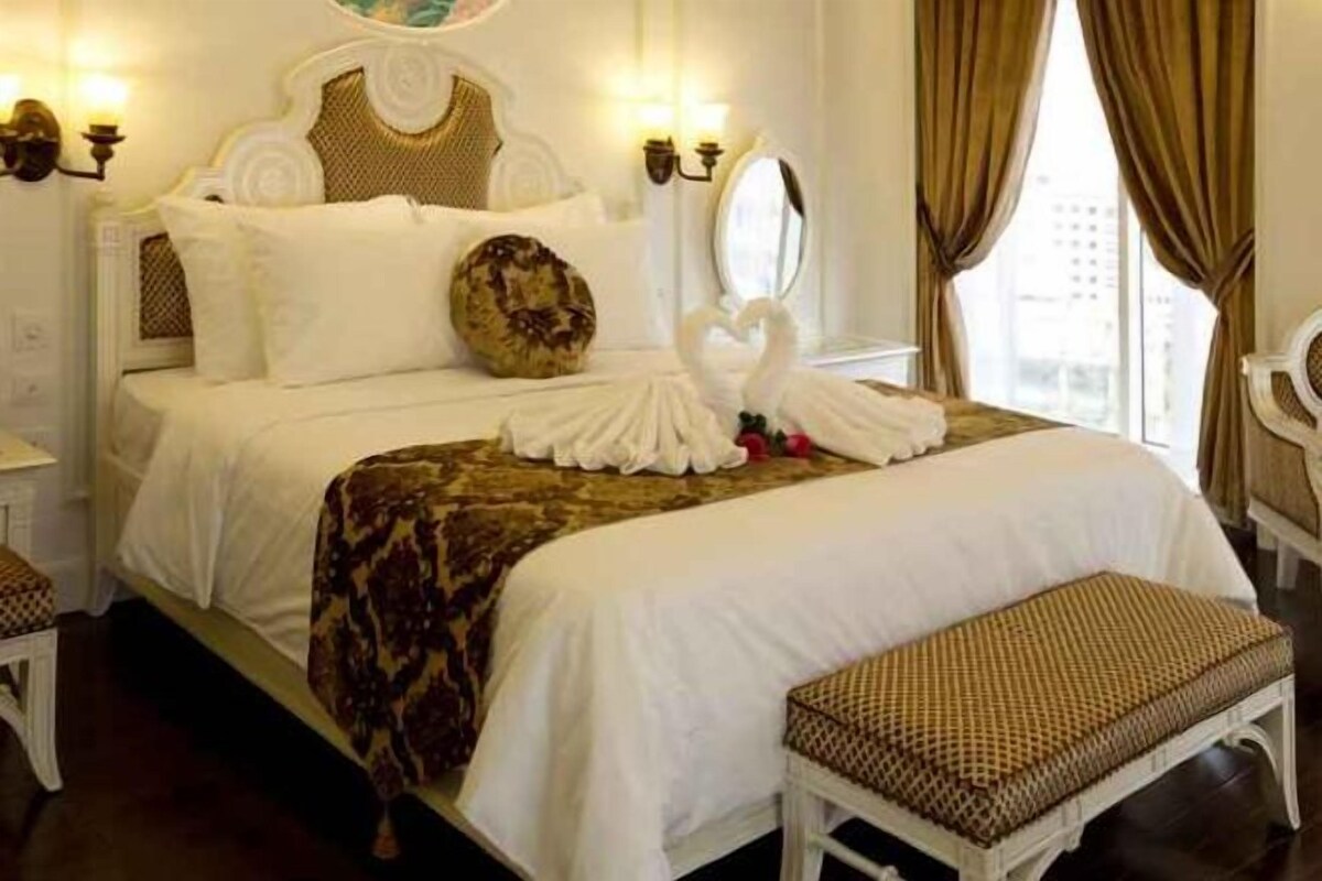 Een hotelkamer met een groot bed, nachtkastje, stoel en raam met gordijnen.