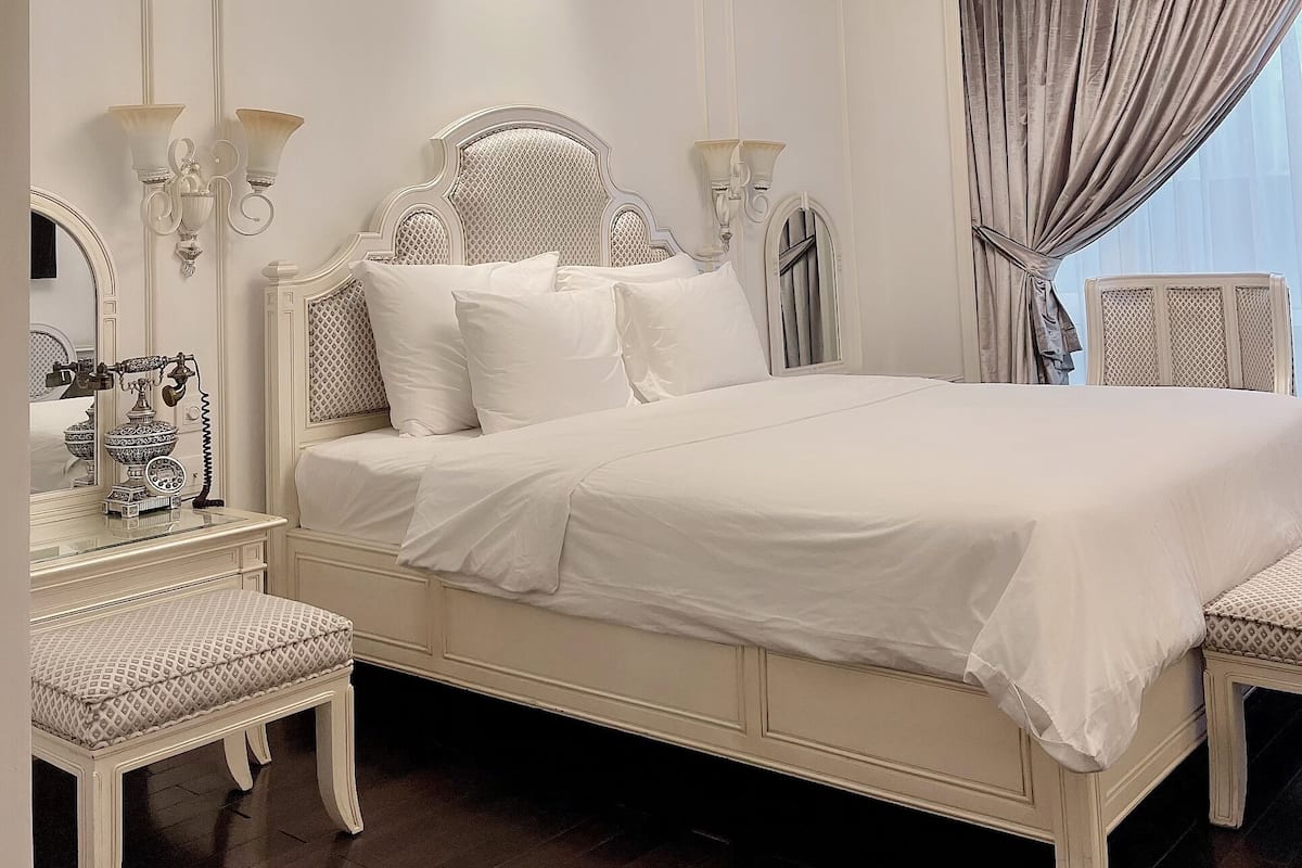 A large bed with white bedding, a chandelier, and a window with curtains.