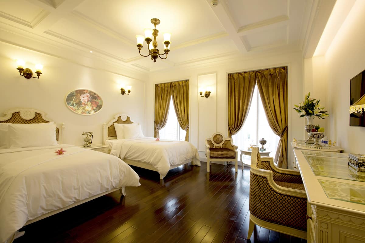 A hotel room with two beds, a sitting area with a chair, a dining table, and a chandelier.