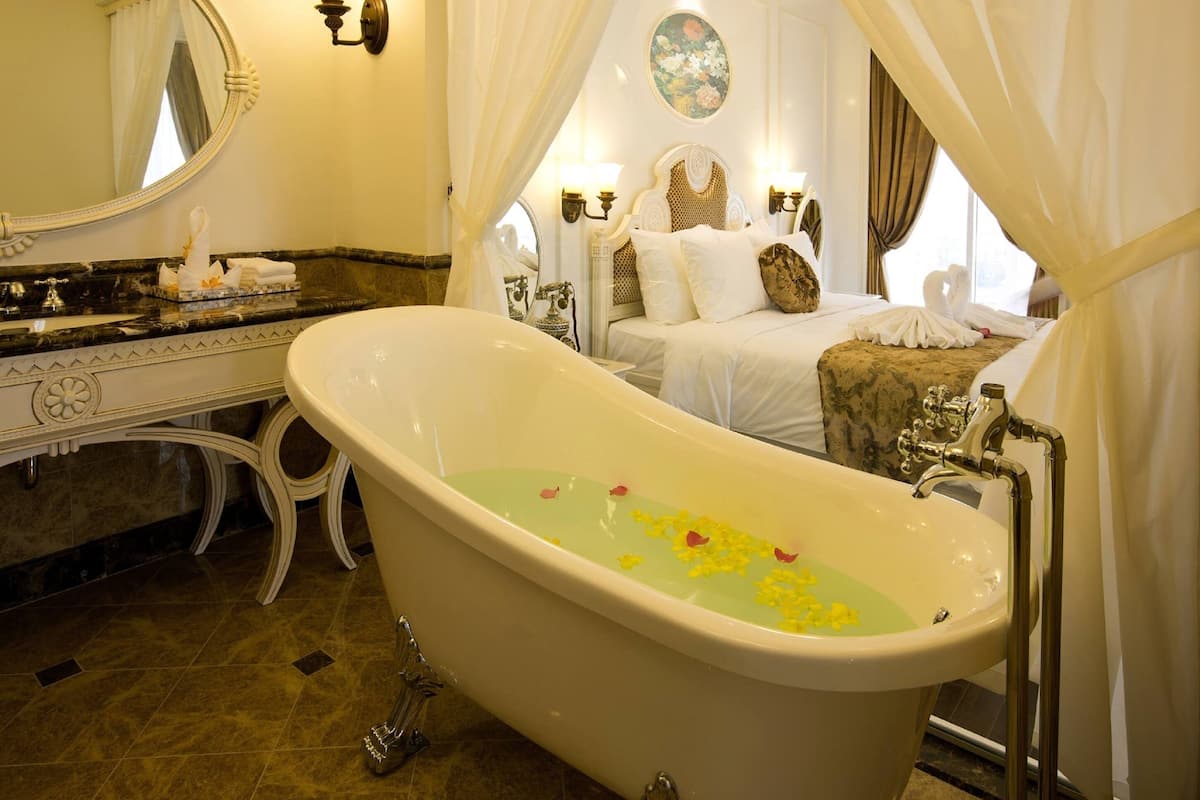 A classic bathroom with a freestanding bathtub, a vanity with a mirror, and a bed with a canopy.