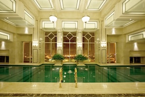 An indoor swimming pool with a view of the cityscape through large windows, surrounded by a luxurious interior with geometric wall designs and modern lighting fixtures. - Eldora Hotel (Hue)
