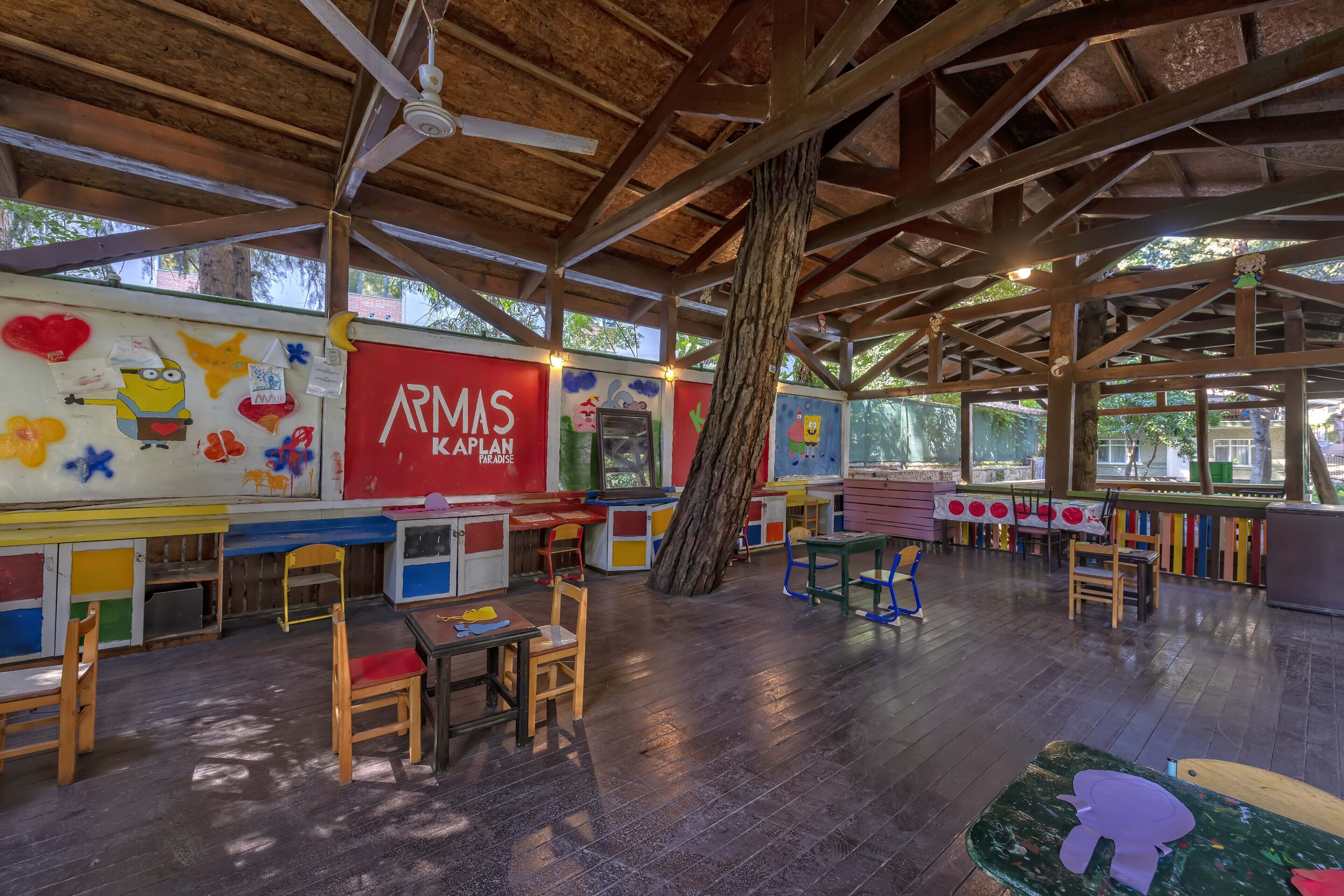 Un área de juegos para niños con paredes de colores, mesas y sillas de madera.