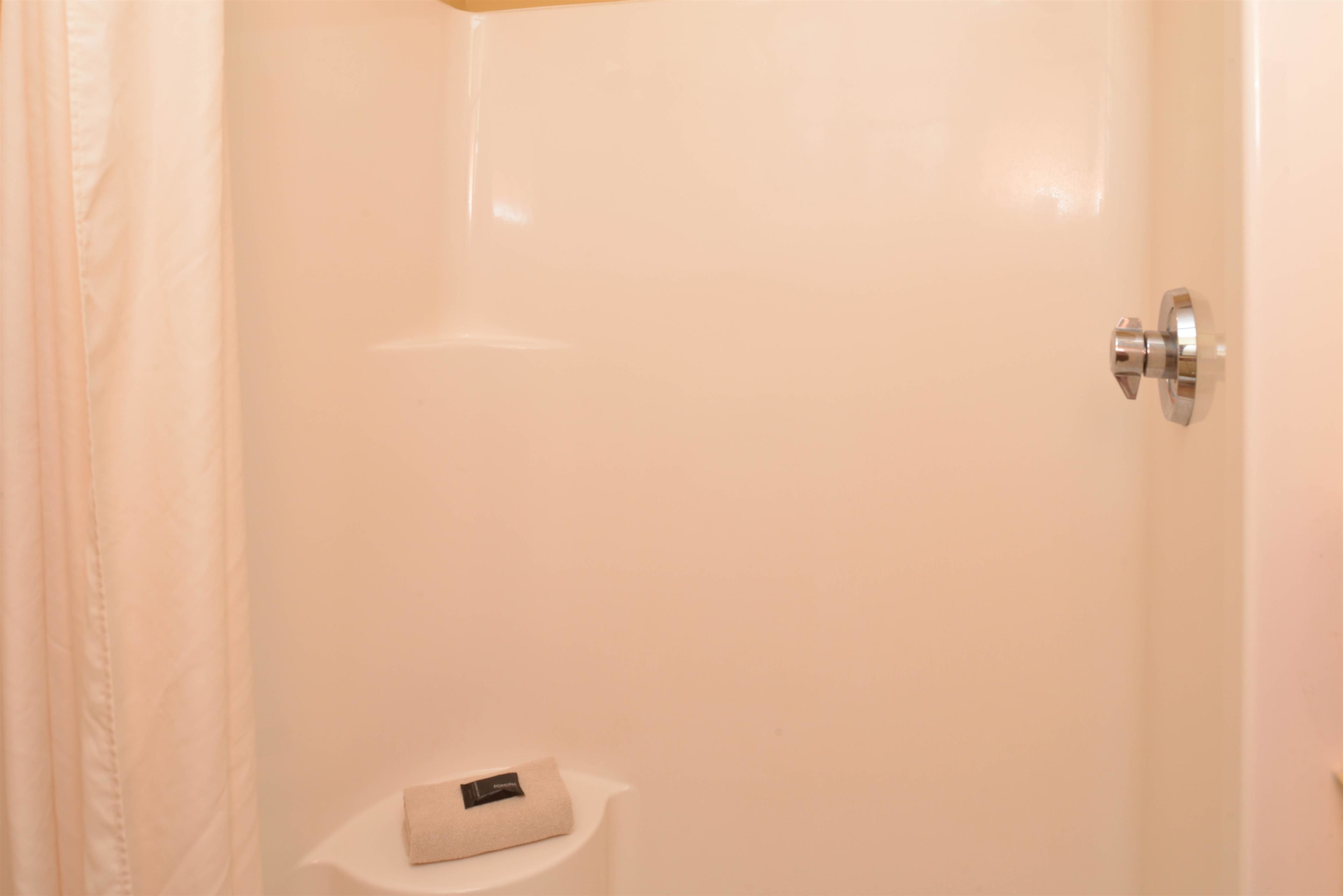 A bathroom with a white shower, a small shelf with a towel, and a metallic door handle.