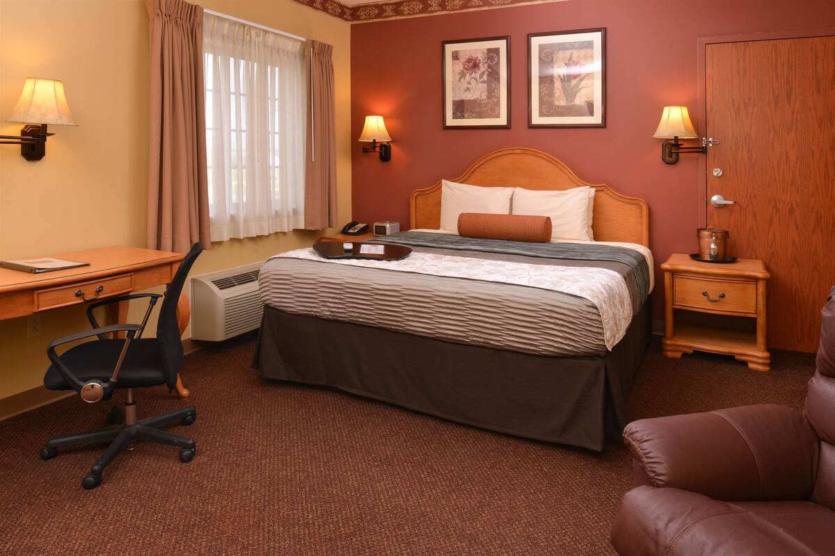 Une chambre d’hôtel équipée d’un lit, d’un bureau, d’une chaise, de tables de chevet, de lampes et d’œuvres d’art accrochées aux murs.