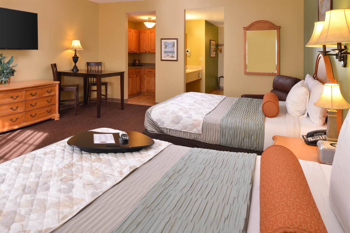 Une chambre d’hôtel avec deux lits, un bureau, une commode et une salle de bain visible à travers une porte ouverte.