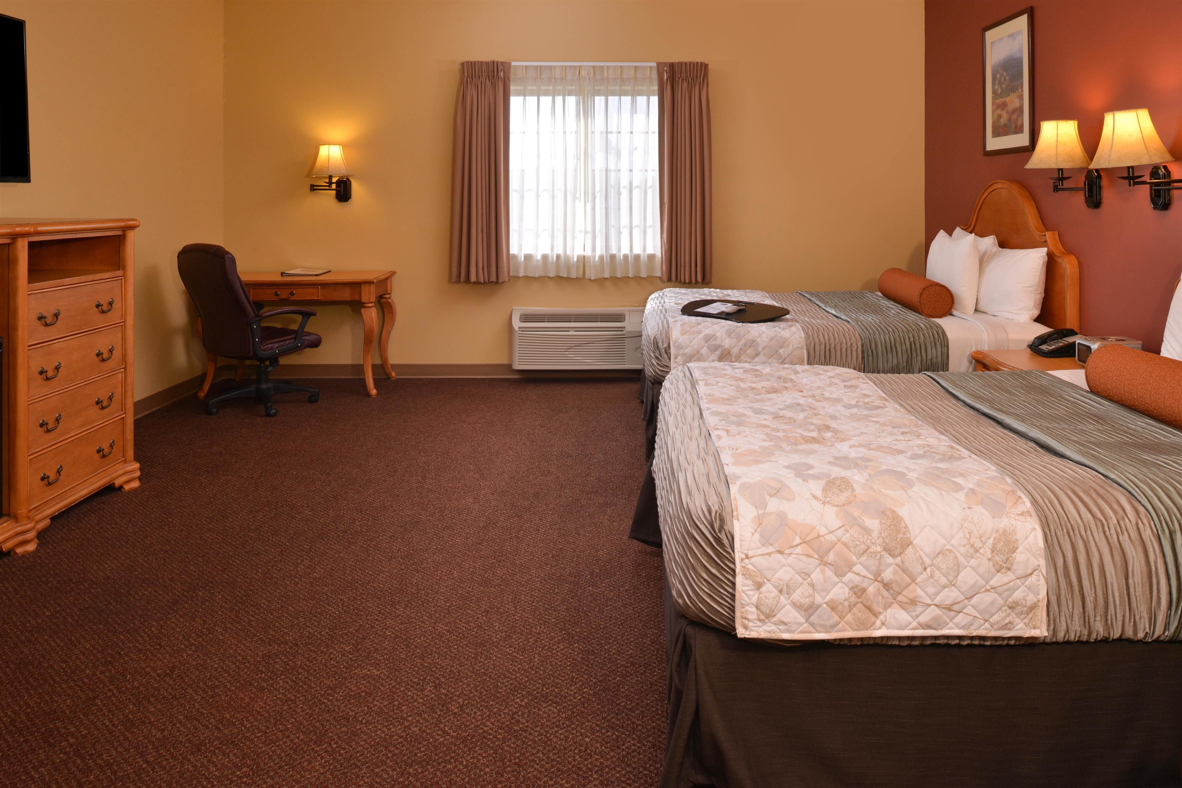 Une chambre d’hôtel avec deux lits, un bureau, une chaise, une commode et une fenêtre avec des rideaux.
