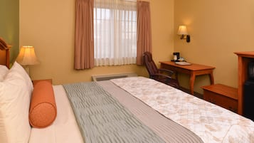 A hotel room with a bed, a desk, a chair, a lamp, and a heater.