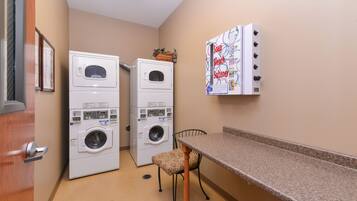 Une buanderie équipée de deux machines à laver et deux sèche-linge superposés, d’une chaise et d’un tableau d’affichage où sont accrochées des notes relatives au linge.