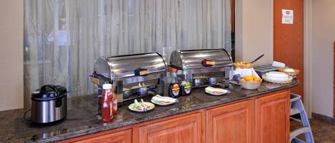 A buffet setup with a stainless steel pot, condiment bottles, and a variety of food items on a counter.