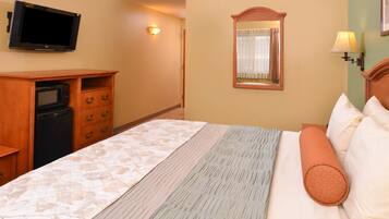 A hotel room with a bed, a TV mounted on the wall, a mirror, and a small desk with a microwave.