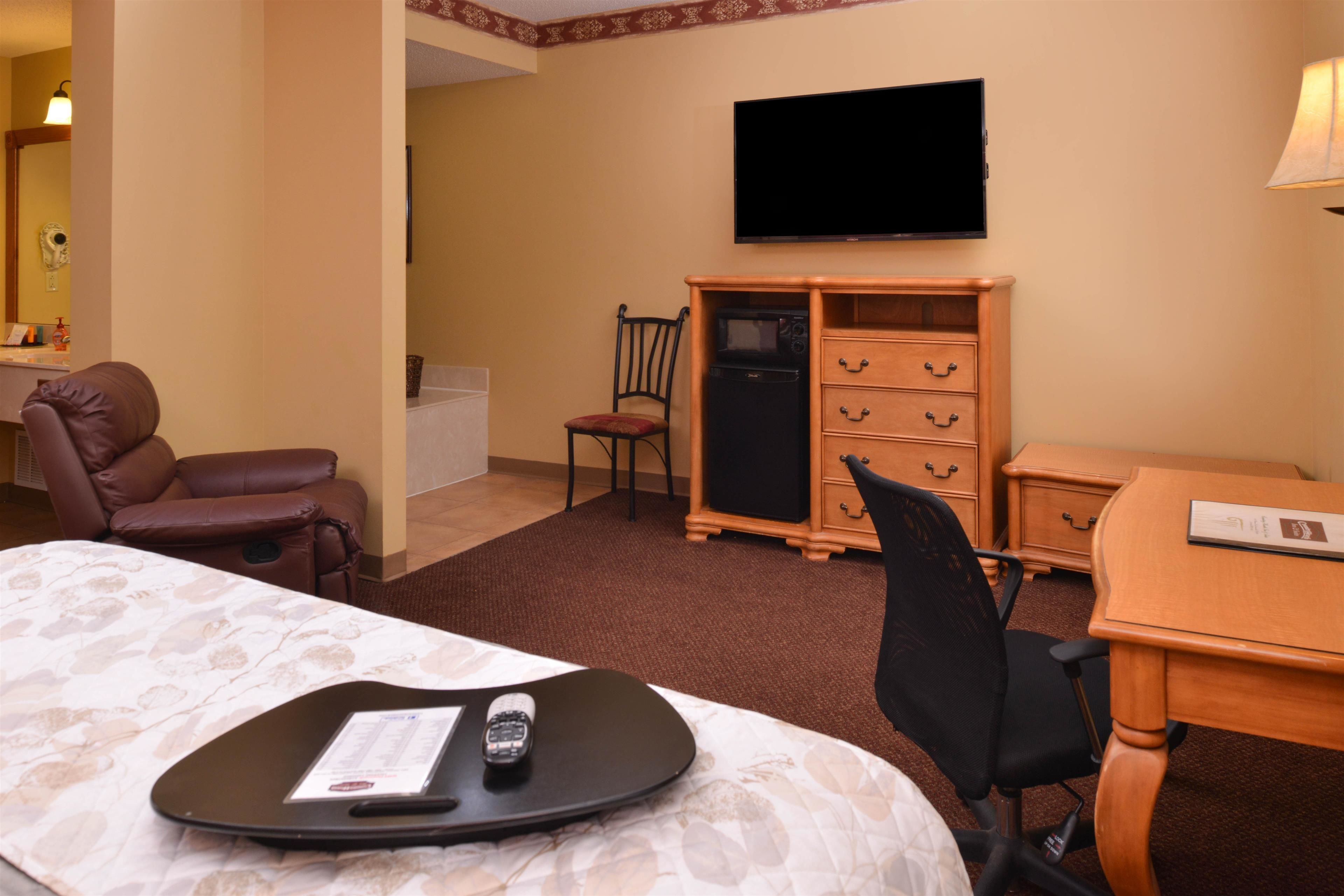 A hotel room with a bed, a desk, a chair, a television, and a minibar.