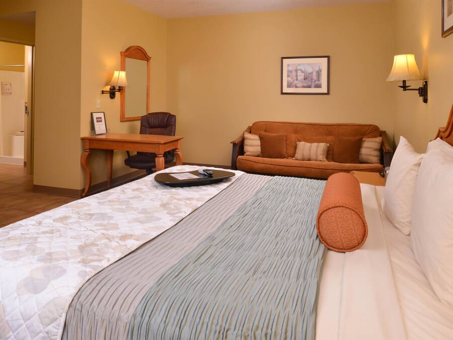 A hotel room with a bed, a desk, a chair, a sofa, and a framed picture on the wall.