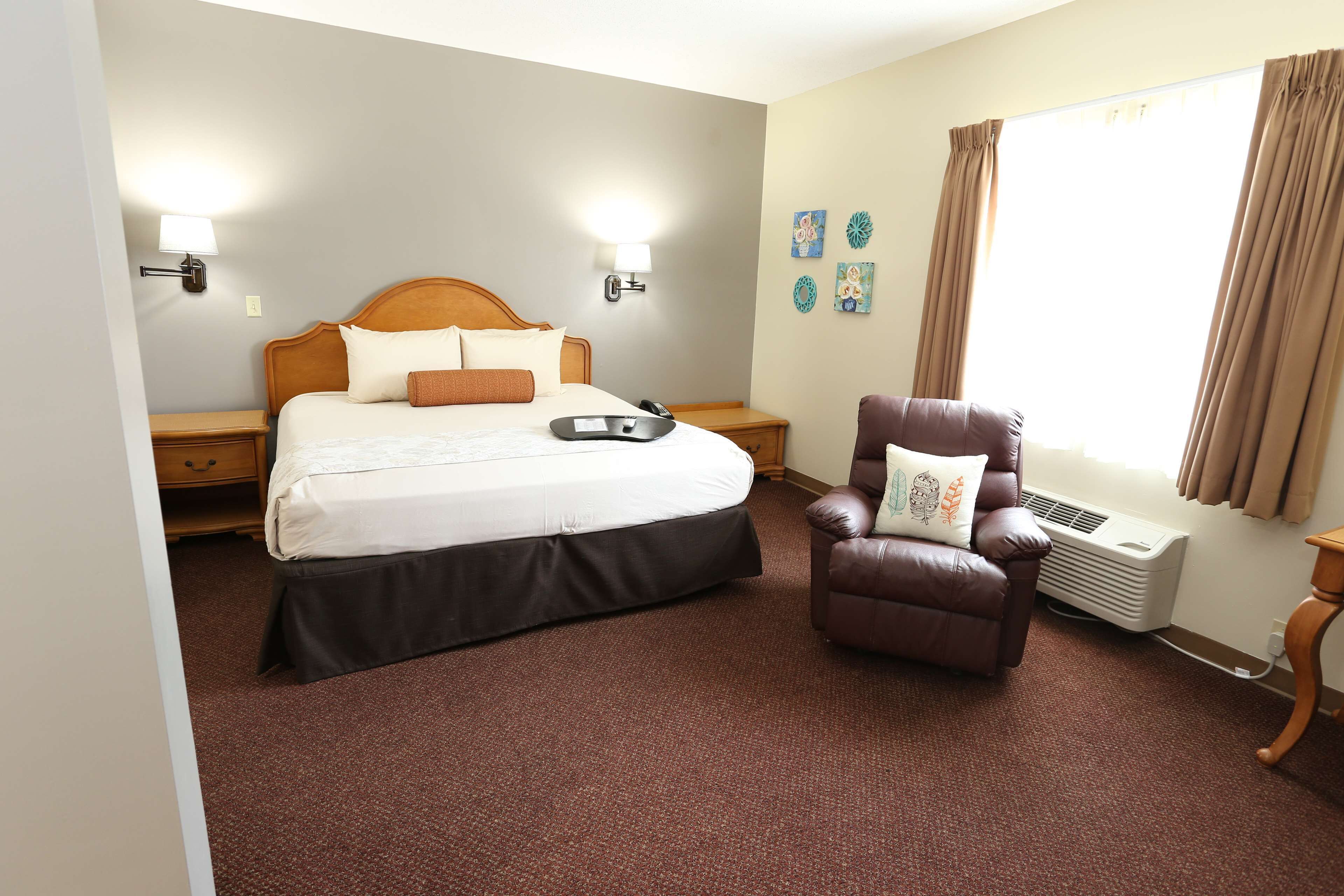 A hotel room with a bed, a chair, a nightstand, a lamp, a heater, and a window with curtains.