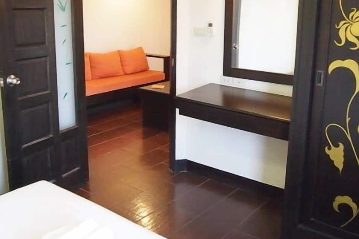 A hotel room with a bed, a desk, and a chair. There is a door with a decorative panel and a wall-mounted air conditioning unit.