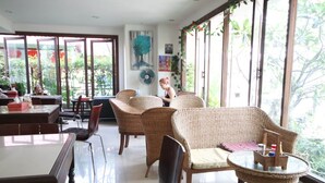 Una habitación amplia con muebles de mimbre, ventanas grandes y un ventilador.
