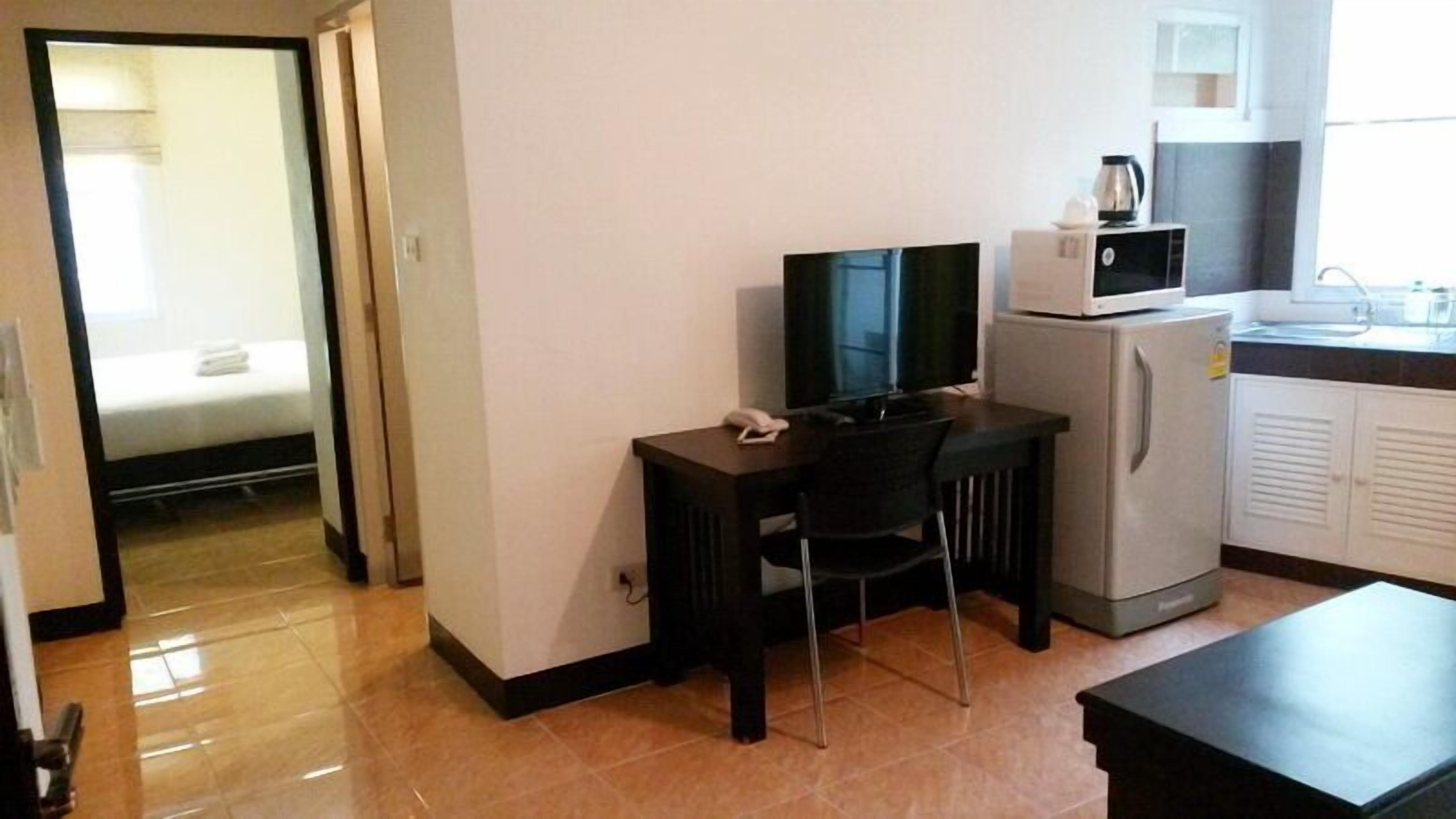 Een compacte hotelkamer met een kitchenette, een televisie, een bureau met stoel en een bed met witte dekbed.