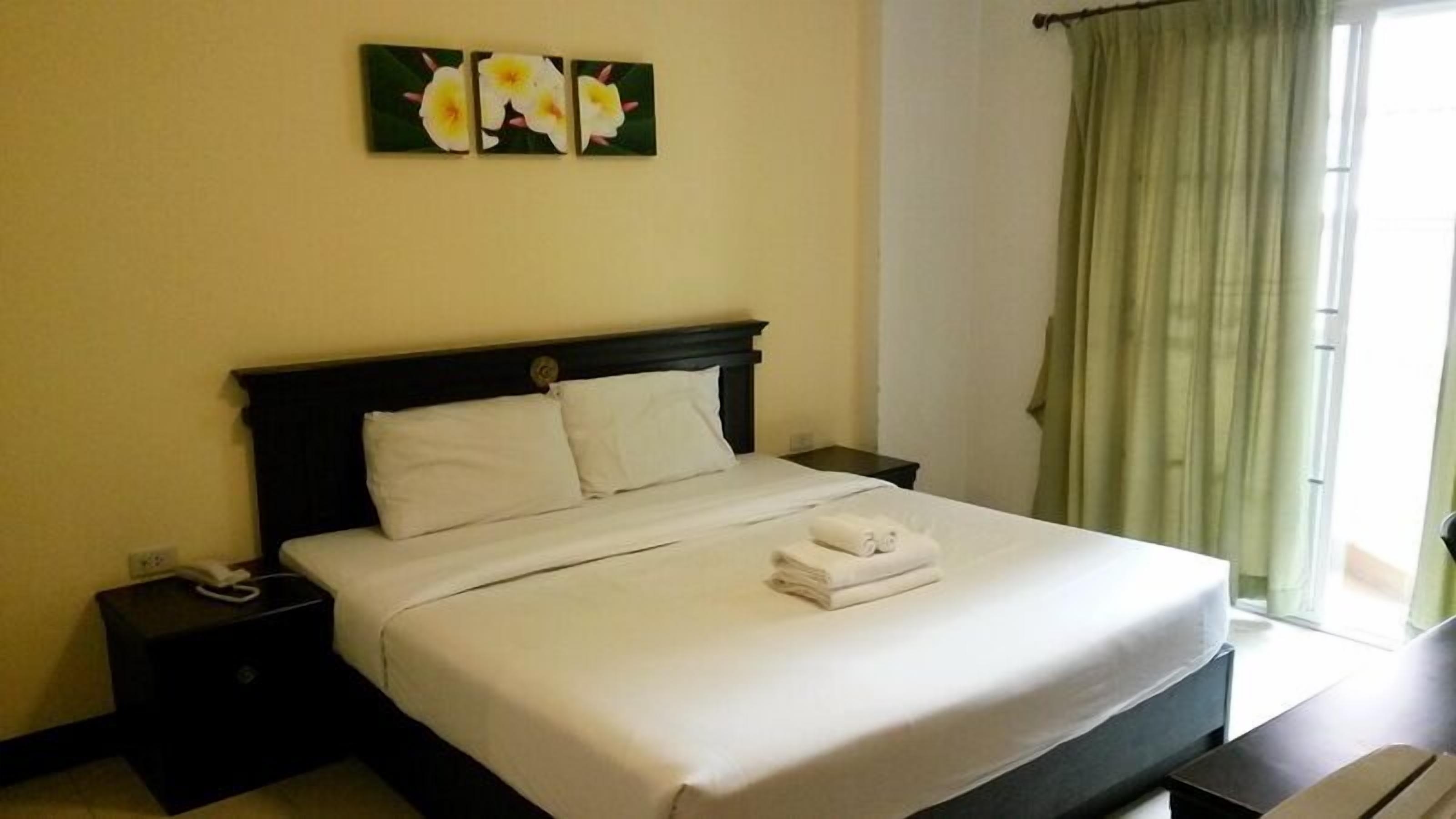 A neatly made bed with white linens and a folded towel, a dark headboard, and a nightstand with a phone.