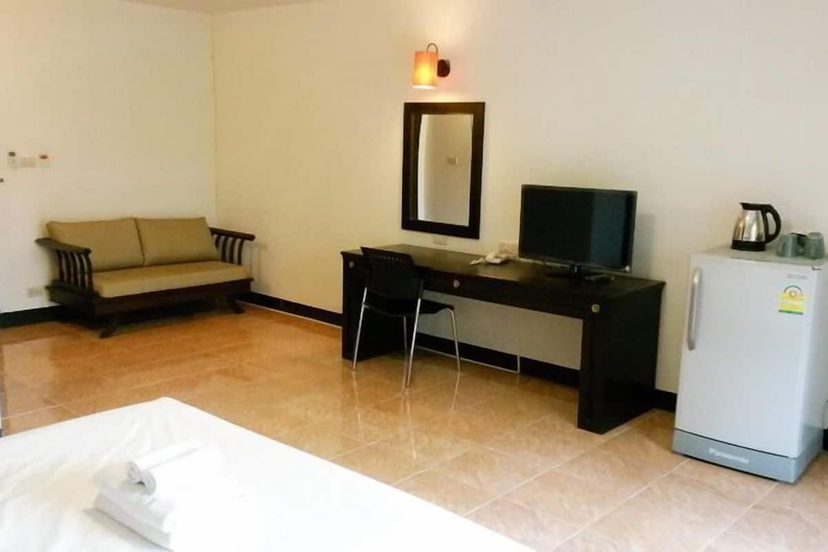 A hotel room with a bed, a desk, a chair, a television, a refrigerator, and a sofa.