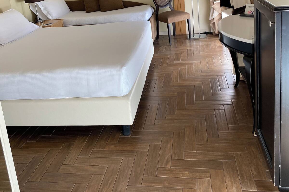 Hotellihuone, jossa on kaksi sänkyä, tuoli, työpöytä, televisio ja lamppu.