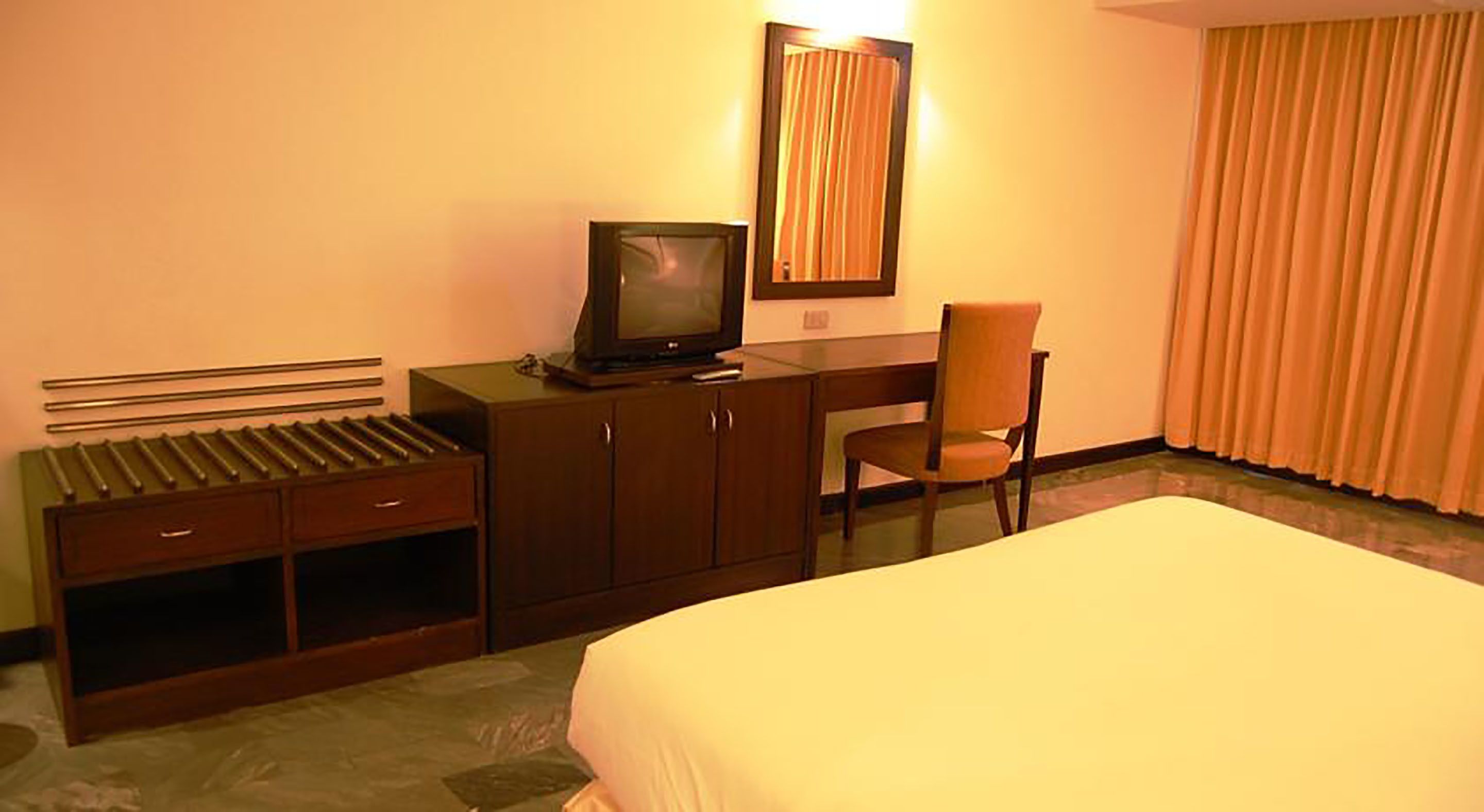 A hotel room with a bed, a desk with a television, a chair, and a window with curtains.