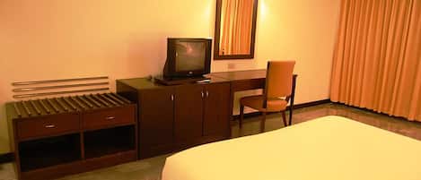 Habitación de hotel con una cama, un escritorio con televisor, una silla y una ventana con cortinas.