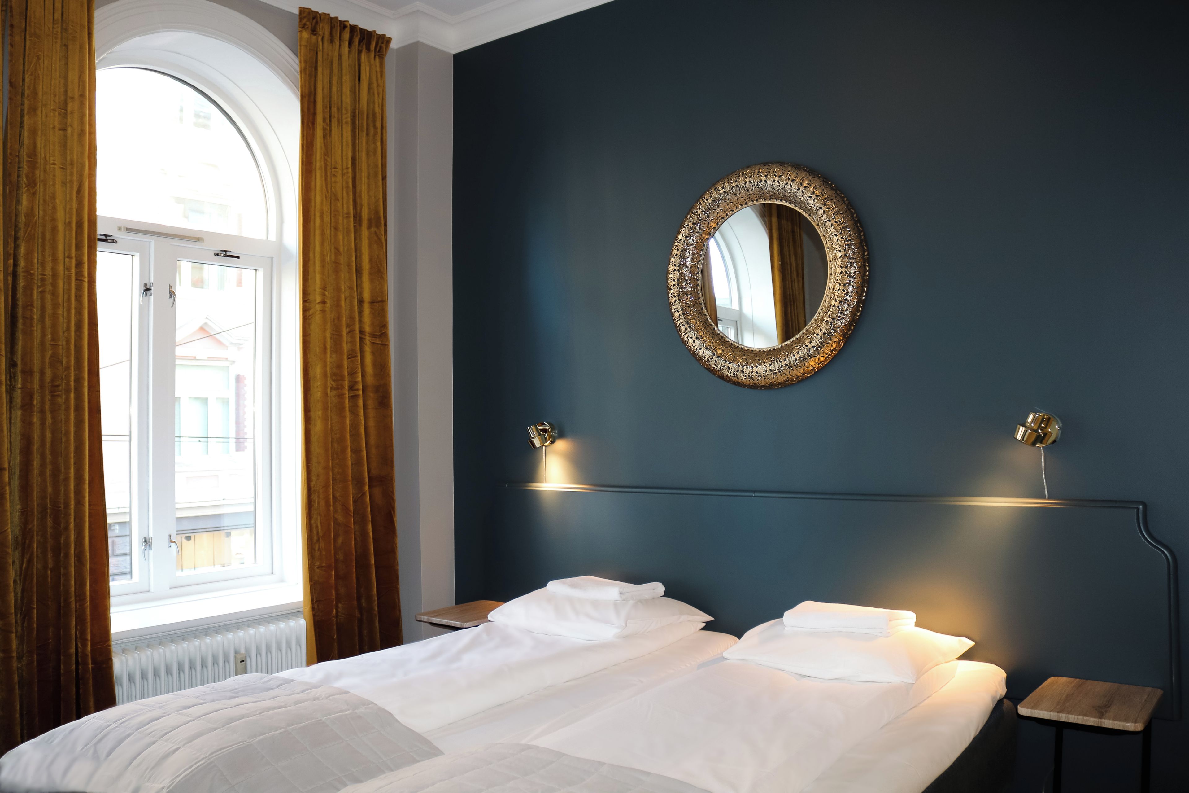 Una habitación de hotel con una cama grande, un espejo redondo y una ventana con cortinas.