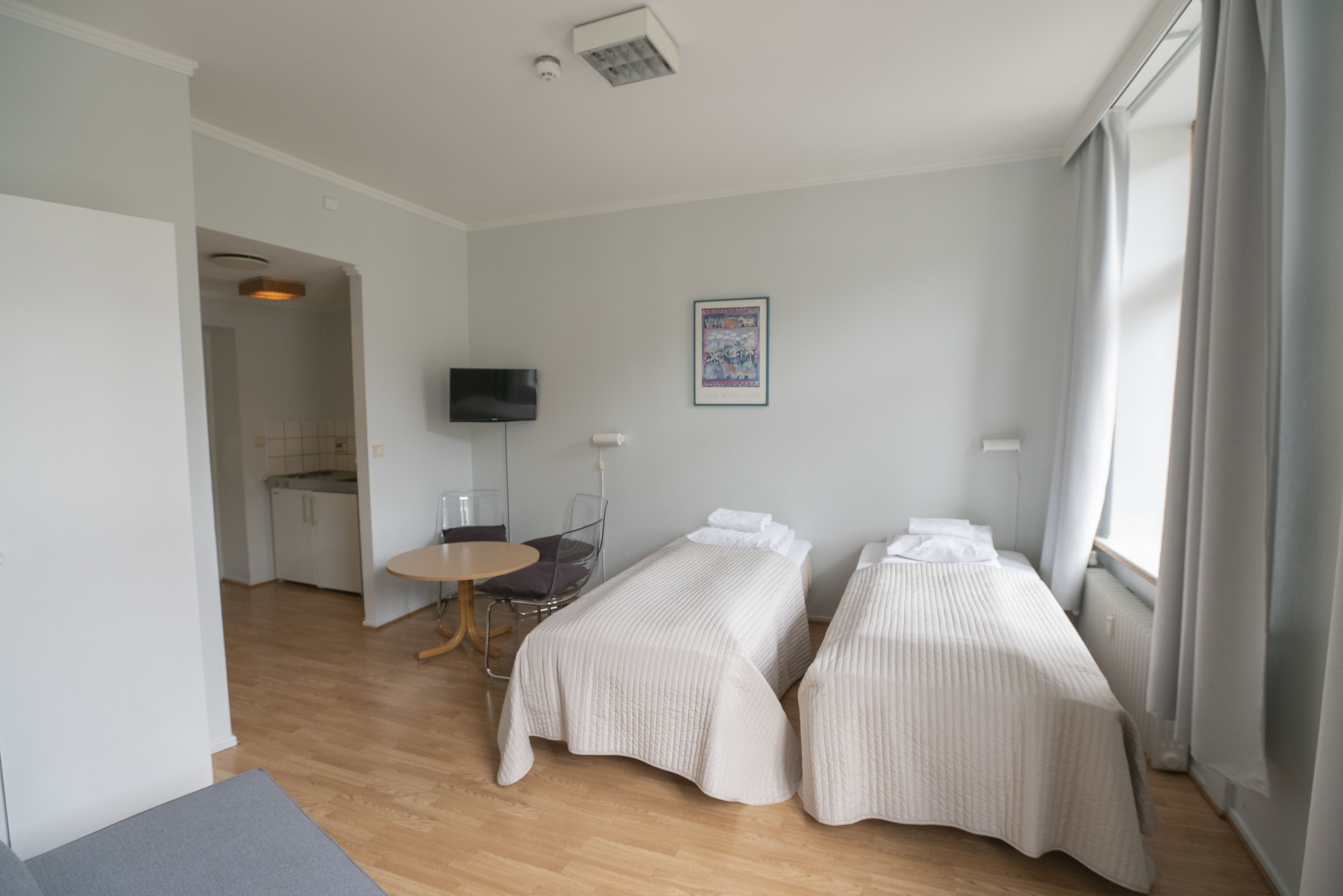 A hotel room with two beds, a TV, a small table, and a view of the outside.