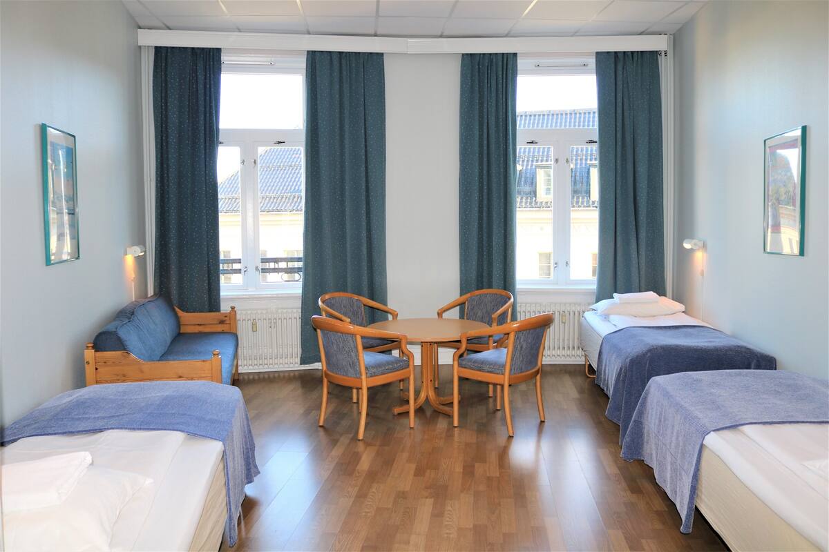 A hotel room with two single beds, a wooden table with chairs, and a sofa.