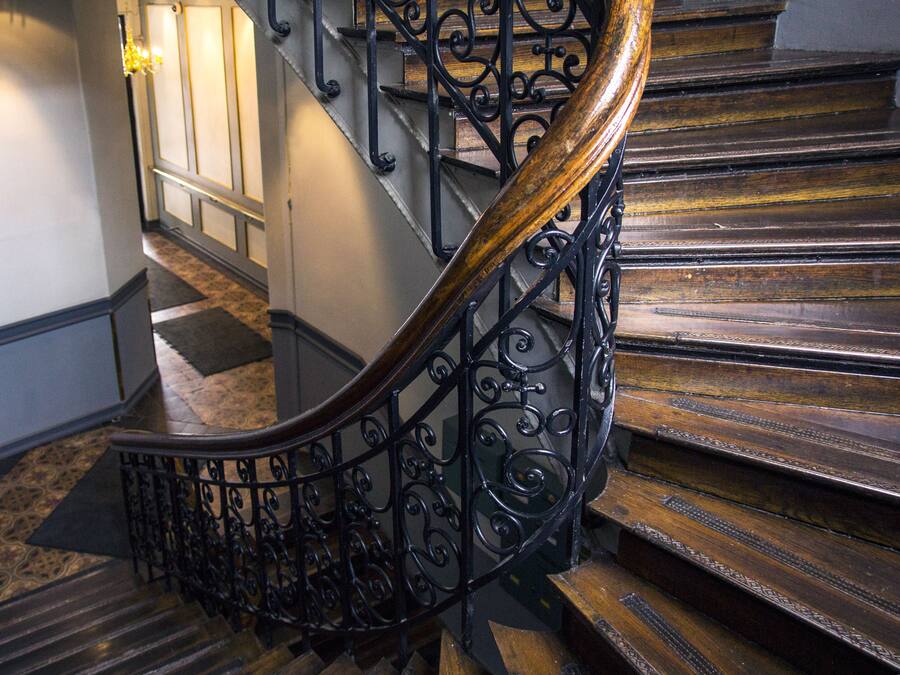 Een houten trap met sierlijk zwart metalen hekwerk en een gepolijste houten leuning.
