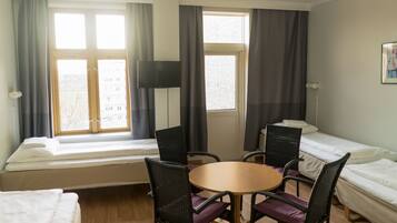 A hotel room with two beds, a round table with chairs, a television, and large windows with curtains.