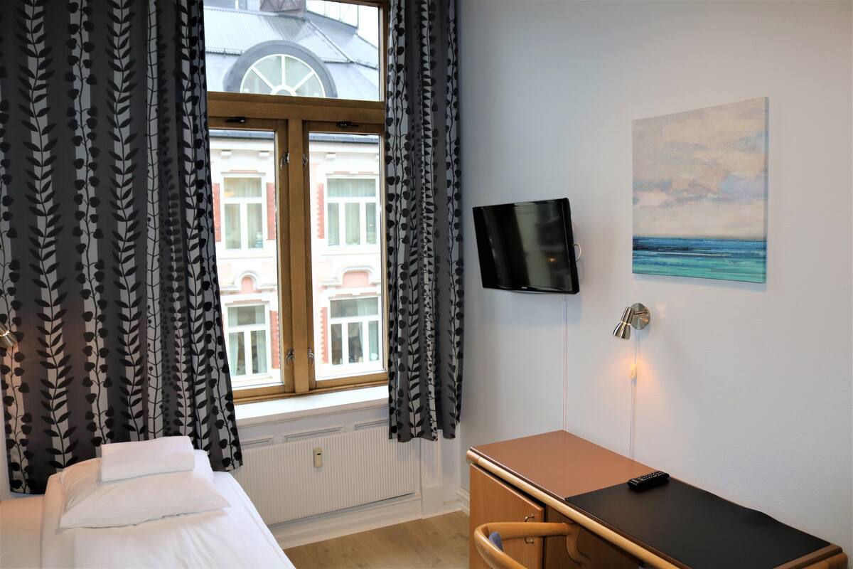 A hotel room with a bed, a desk, a TV, and a window with curtains.