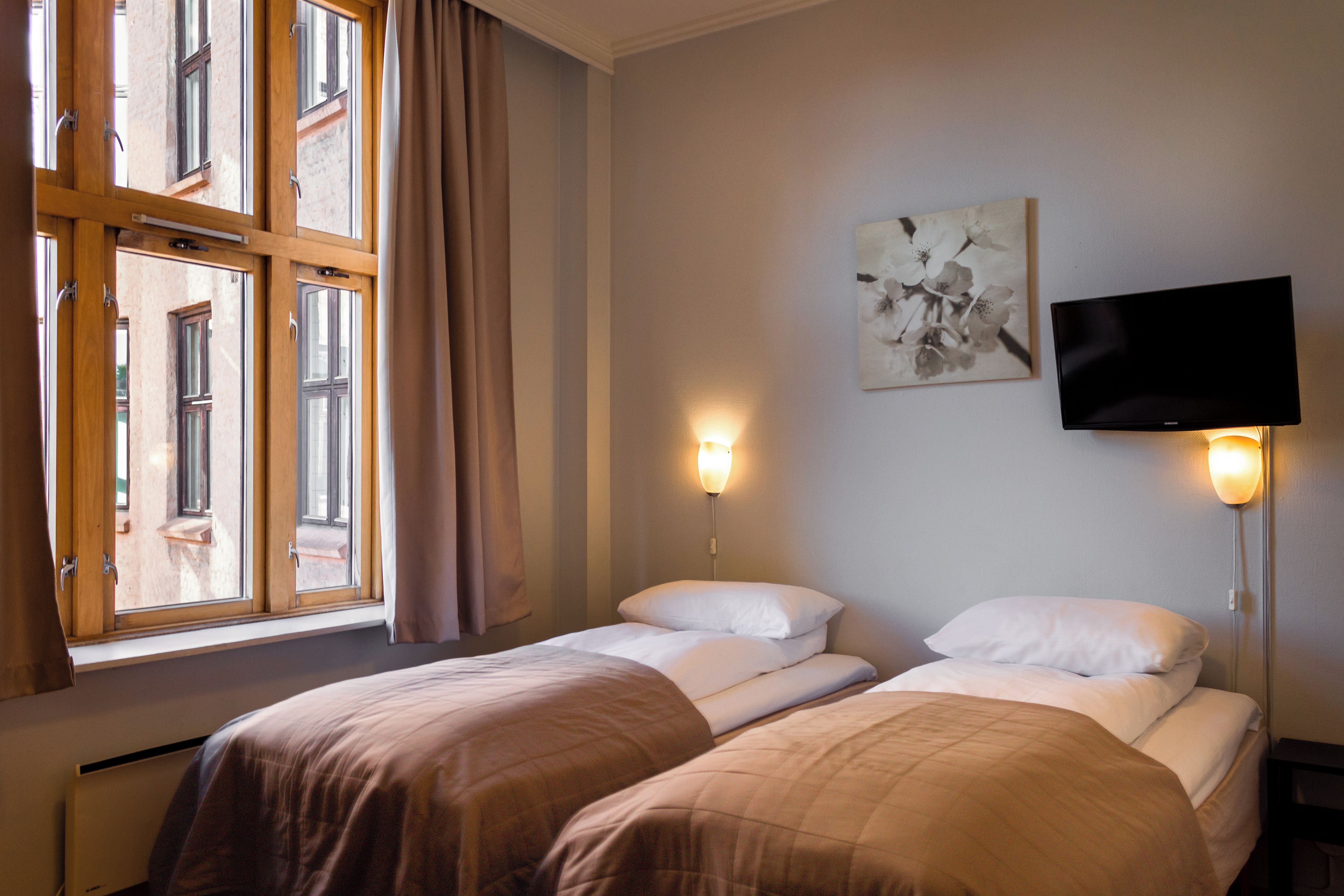 A hotel room with two beds, a flat-screen TV mounted on the wall, and a window with curtains.