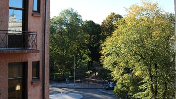 A building with multiple windows and balconies, a street with cars, and trees in the background.