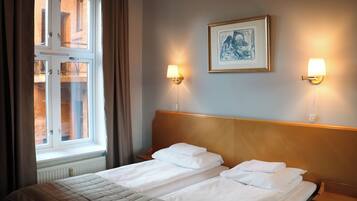 A hotel room with a double bed, two bedside lamps, a framed artwork on the wall, and a window with curtains.