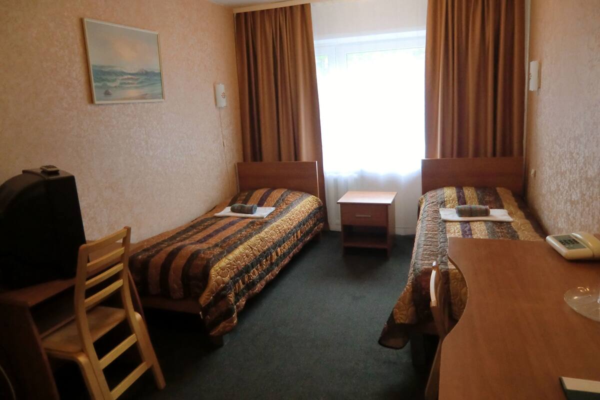 Ein Hotelzimmer mit zwei Einzelbetten, einem Schreibtisch, einem Sessel, einem Fernseher und einem Bild an der Wand.