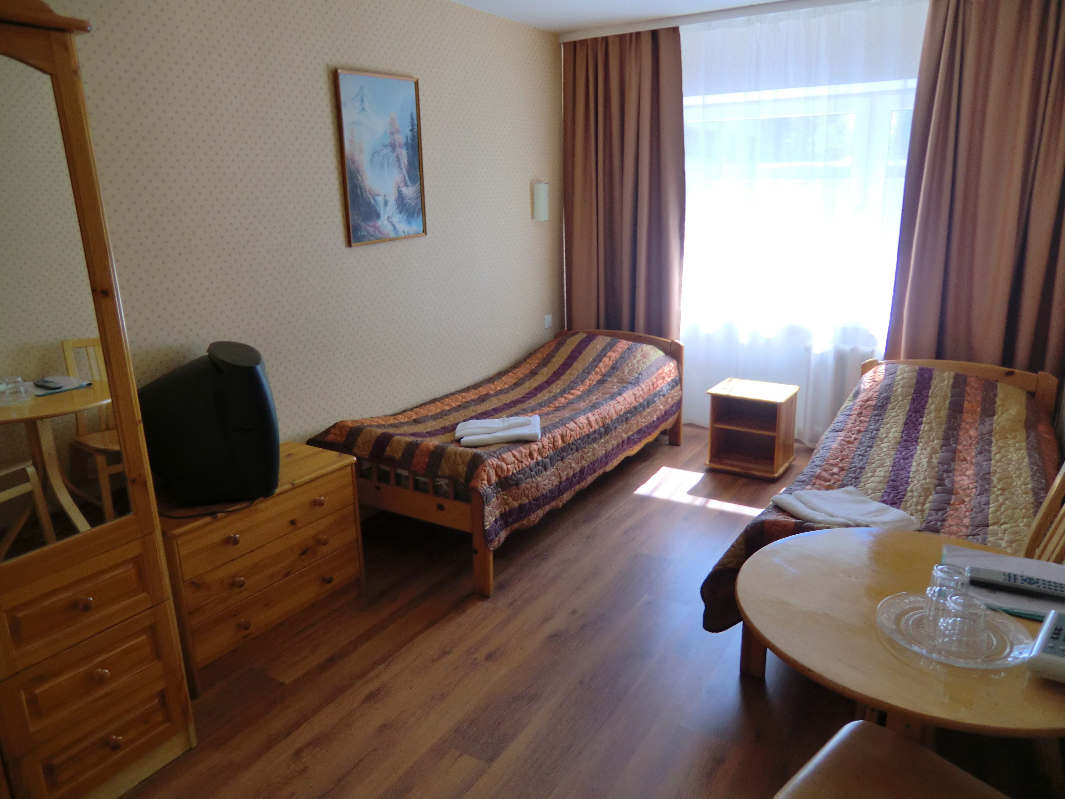 A room with a bed, a wooden dresser, a small table with a glass top, and a chair.