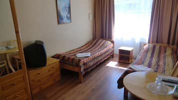A room with a bed, a wooden dresser, a small table with a glass top, and a chair.