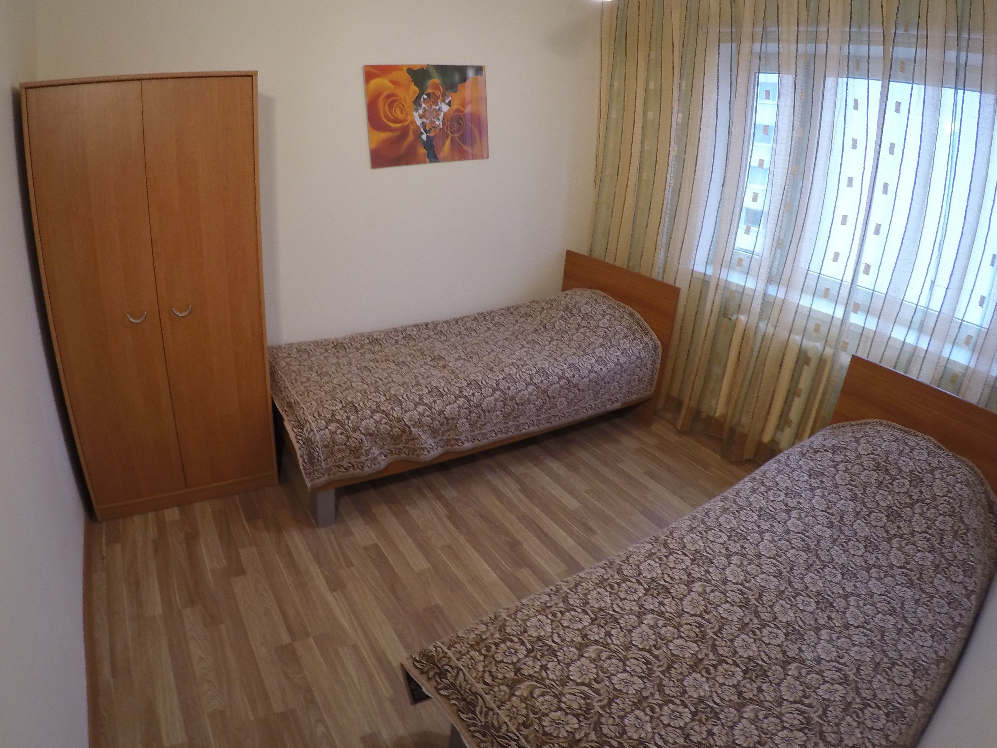 A room with two single beds, a wooden wardrobe, and a painting on the wall.