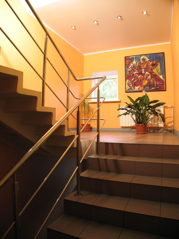 A staircase with metal railings leading to a landing area with a potted plant and a painting on the wall.