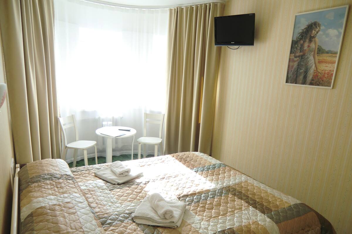 Ein Hotelzimmer mit Bett, Wandfernseher, einem Gemälde und einem Tisch mit Stühlen.