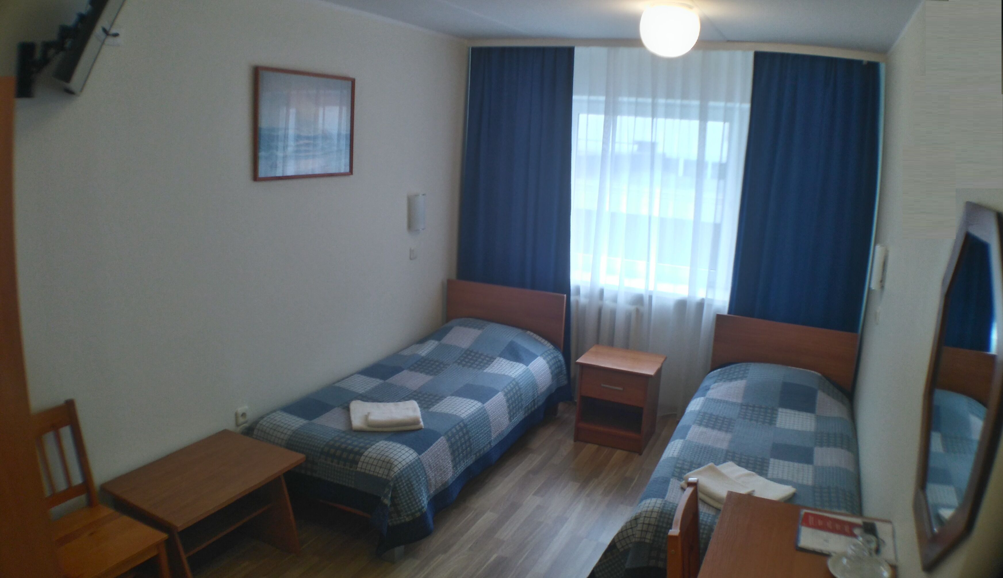 Een kleine, net kamer met twee eenpersoonsbedden, een houten bureau, een stoel en een klein tafeltje.
