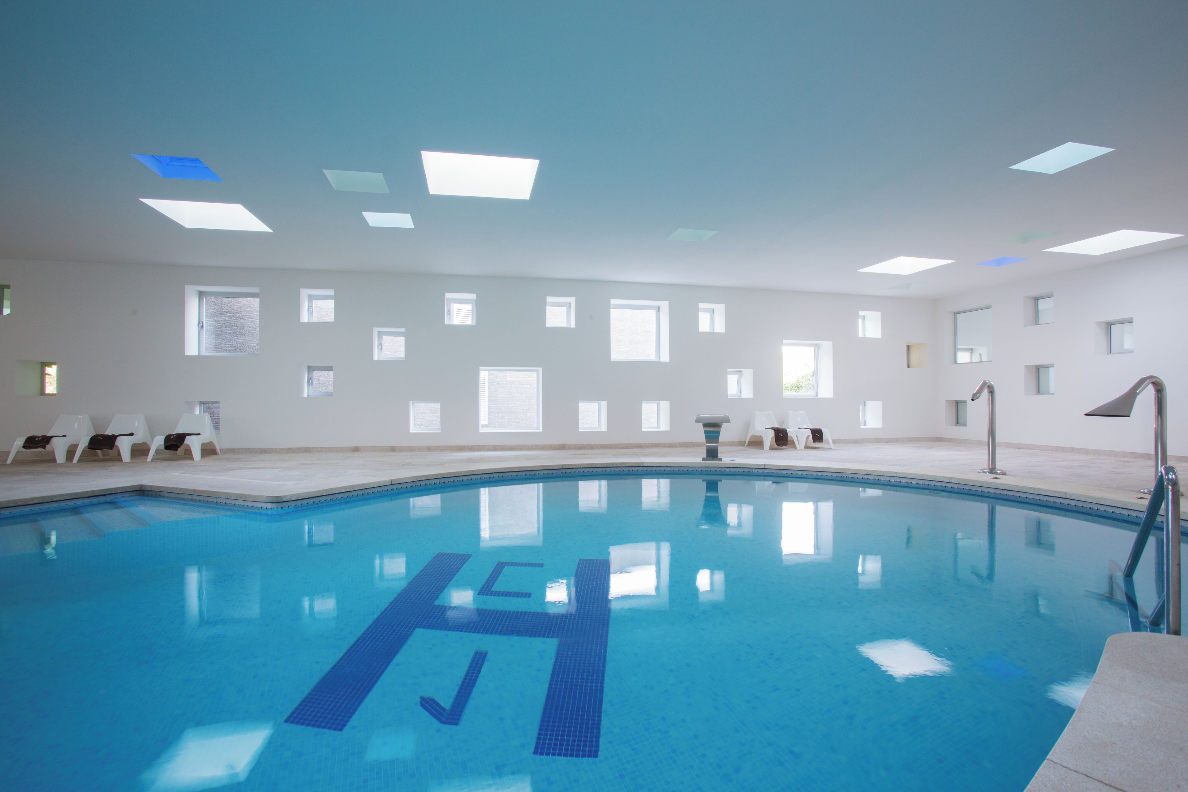 A large indoor swimming pool with clear blue water, marked lanes, and a lifeguard stand.
