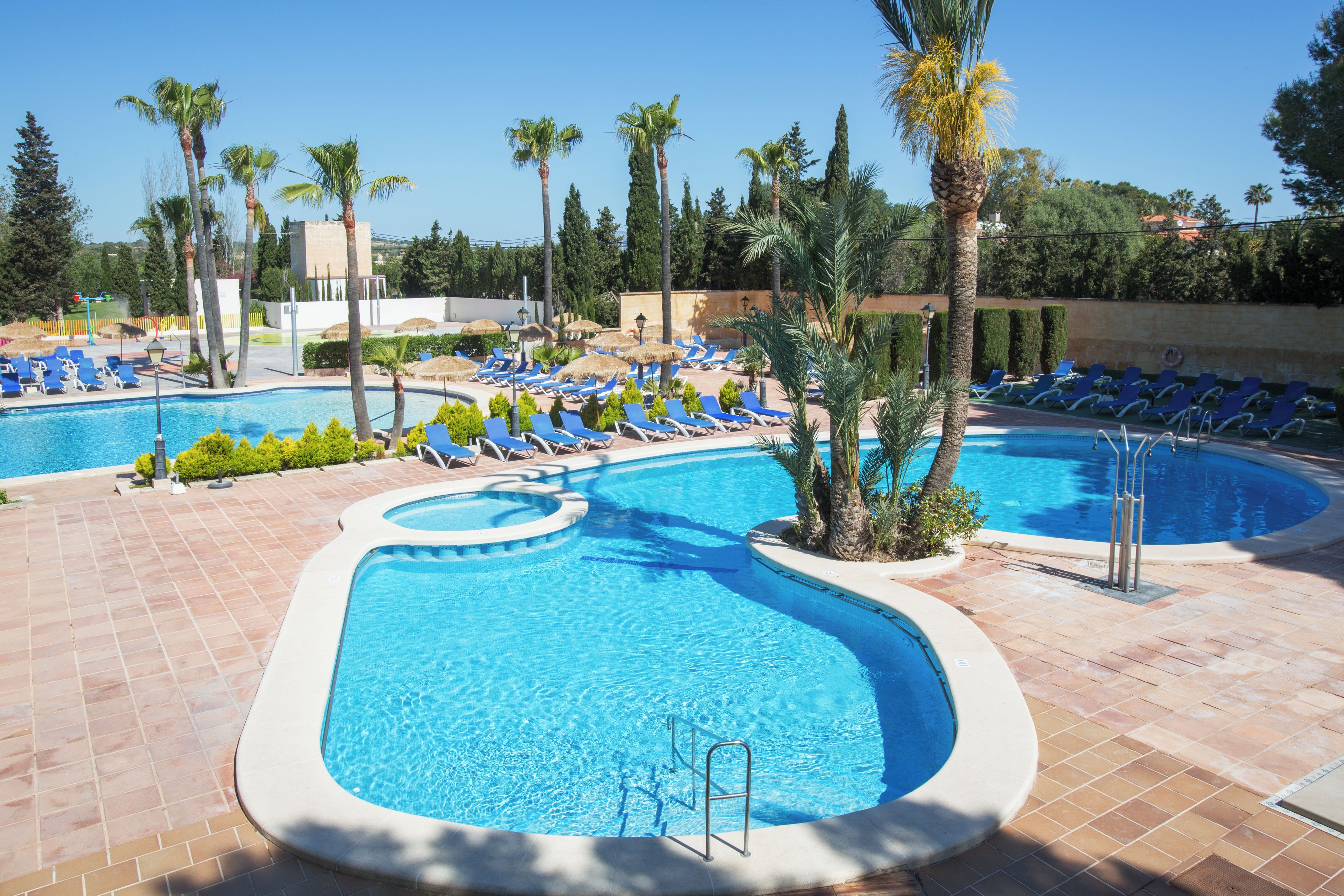 Un área de piscina con varios sitios para tomar el sol y una piscina azul cristalina.