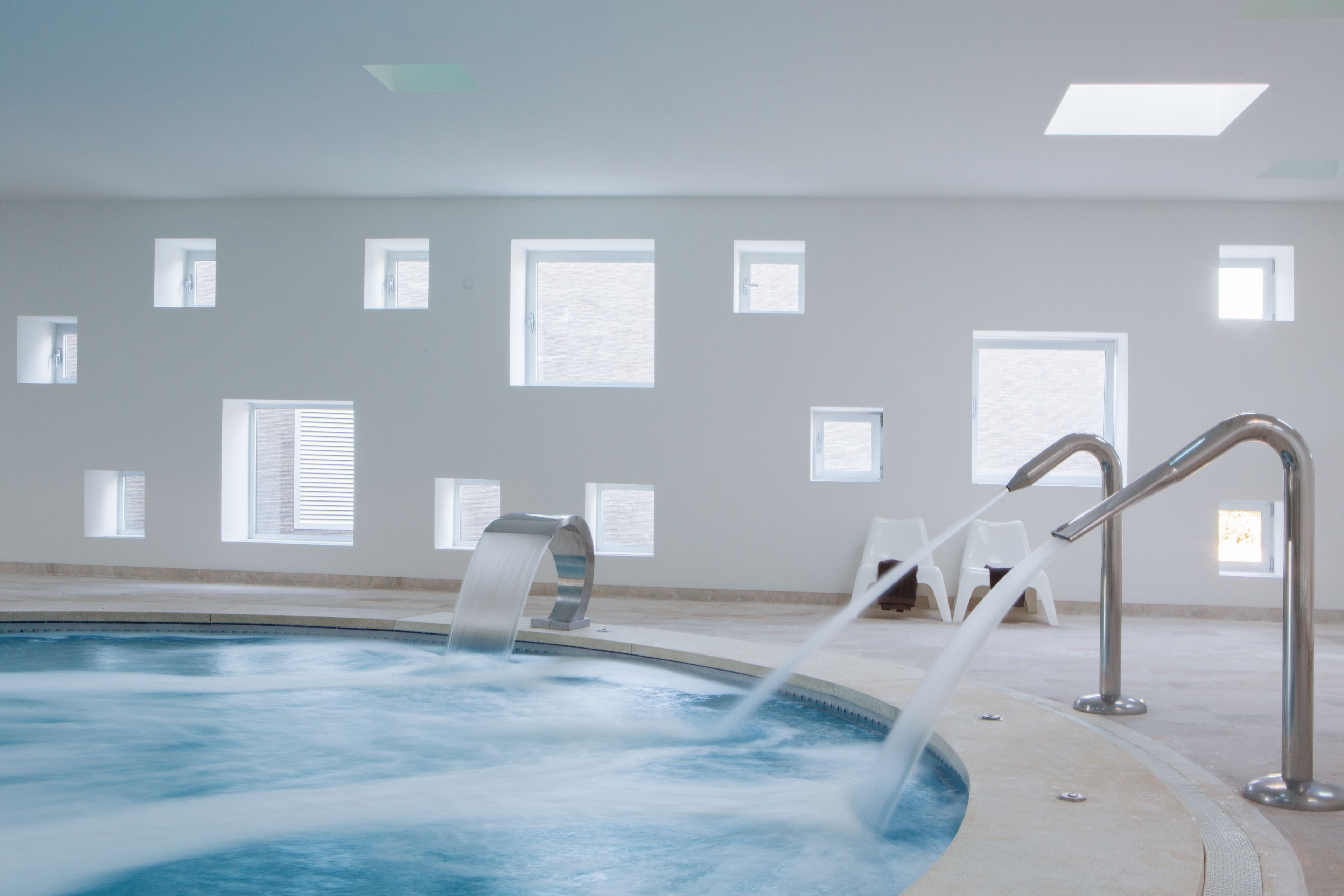 Una piscina con agua cristalina, rodeada de un suelo de baldosas y paredes blancas.